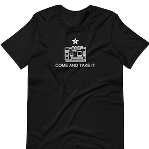 Puede incluir: Camiseta negra con un contorno blanco de una placa de circuito y una estrella con la letra B en su interior. El texto "COME AND TAKE IT" está impreso debajo de la placa de circuito.