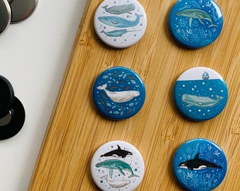 May include: Set of 8 blue and white whale and ocean themed pinback buttons. Each button features a different whale design with a white background and blue accents.