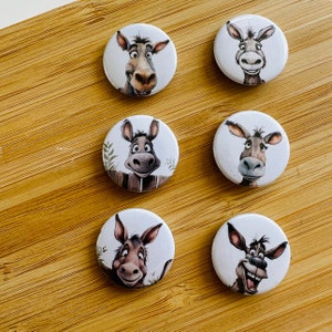 Op de afbeelding: Zes ronde witte knoppen met afbeeldingen van cartoon-ezels. Elke ezel heeft een andere uitdrukking en wordt afgebeeld in een andere pose.