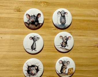 May include: Six round white buttons with different illustrations of mice. The mice are depicted in various poses, including peeking out of a hole, holding a piece of cheese, and looking sad.
