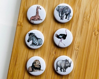 May include: Six white round buttons with different animal illustrations. The animals are a giraffe, an elephant, a zebra, an ostrich, a lion, and a rhinoceros.
