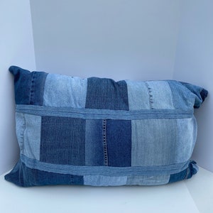 May include: A blue denim pillow with a patchwork design. The pillow is made from different shades of blue denim and has a rectangular shape.