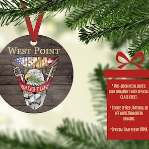 May include: A round metal ornament featuring a dark wood grain background and the West Point USMA crest. The design includes a bald eagle, an American flag, crossed swords, and the text West Point, USMA, and Hold The Line. A red ribbon is attached.