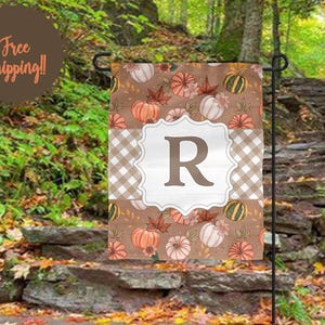 May include: A rectangular garden flag featuring a brown background with a pattern of orange, white, and green pumpkins and autumn leaves. A central white scalloped frame displays a large brown letter R over a light brown and white gingham pattern.