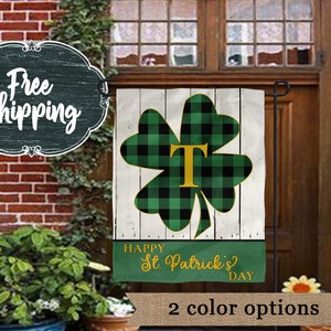 May include: A green and black checkered shamrock with a gold letter "T" in the center. The shamrock is on a white wooden background with the text "Happy St. Patrick's Day".