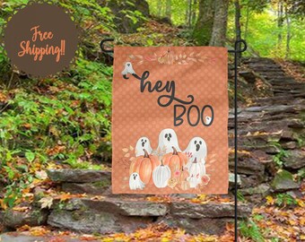 May include: A Halloween-themed garden flag with a brown and orange background. The flag features a group of white ghosts with the text "Hey Boo" in black lettering. The flag is decorated with fall leaves and pumpkins.