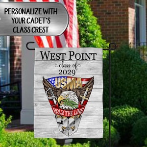 Puede incluir: Una bandera de jardín con el texto "West Point class of 2029" y un emblema de la USMA con un águila, alas y una espada. La bandera también incluye la frase "Hold the Line" y una placa de identificación que dice "Personaliza con la insignia de clase de tu cadete".