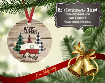 Op de afbeelding: Een ronde, houten kerstversiering met een rode en witte camper, groene en witte geruite bomen en de tekst "HAPPY CAMPERS" en "The Rucder 2022".