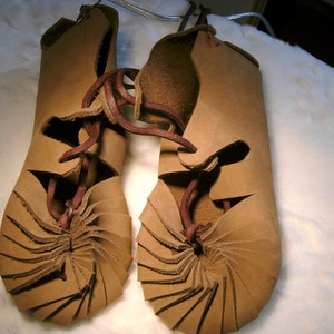 May include: A pair of brown leather sandals with a unique spiral design. The sandals are laced up the front with brown leather laces.