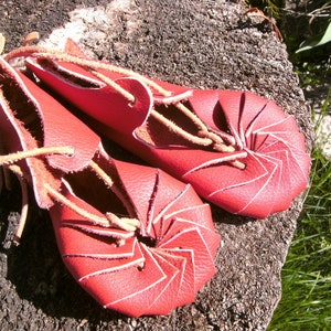 May include: A pair of red leather sandals with a unique spiral design. The sandals are tied with brown leather laces.
