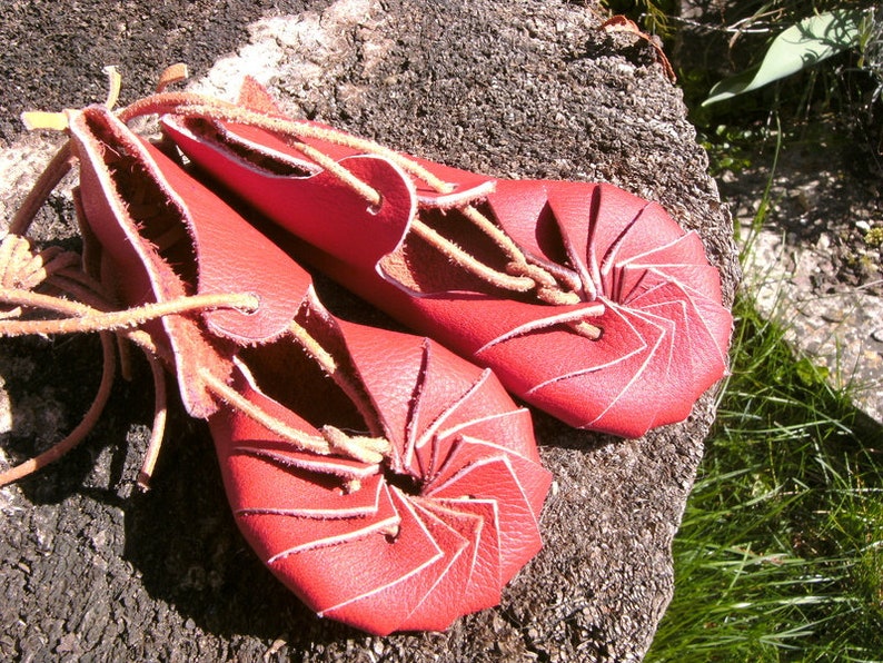 May include: A pair of red leather sandals with a unique spiral design. The sandals are tied with brown leather laces.