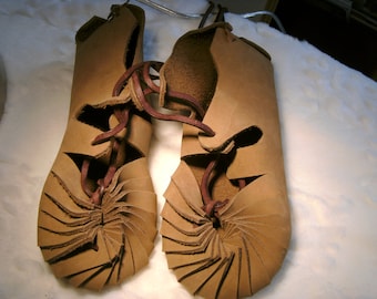 May include: A pair of brown leather sandals with a unique spiral design. The sandals are laced up the front with brown leather laces.
