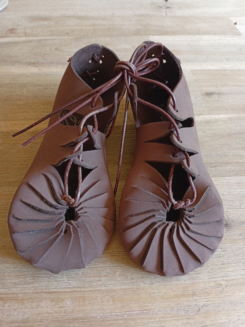 May include: A pair of brown leather sandals with laces. The sandals have a unique design with a circular pattern on the sole.
