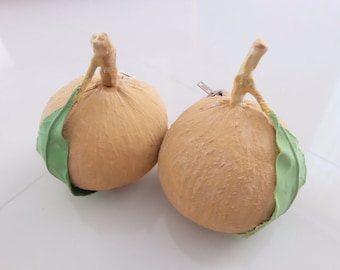 May include: Two decorative coconuts with green leaves attached. The coconuts are a light brown color and have a rough texture.