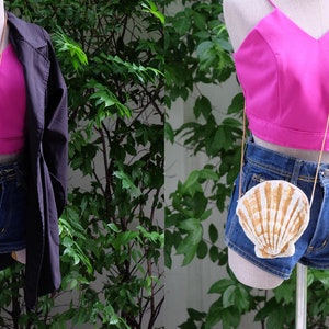 K&ouml;nnte beinhalten: Eine wei&szlig;e und goldene Muschel-f&ouml;rmige Handtasche mit einer goldenen Kettenkette. Die Tasche wird von einer Schaufensterpuppe getragen, die ein rosa Crop-Top und eine Jeans-Shorts tr&auml;gt.