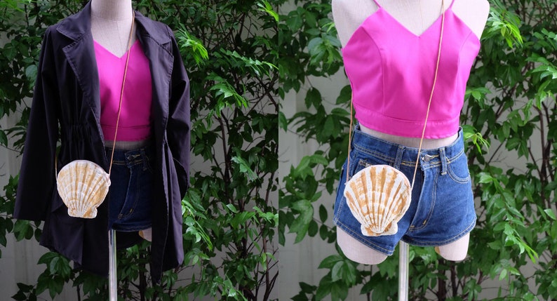 K&ouml;nnte beinhalten: Eine wei&szlig;e und goldene Muschel-f&ouml;rmige Handtasche mit einer goldenen Kettenkette. Die Tasche wird von einer Schaufensterpuppe getragen, die ein rosa Crop-Top und eine Jeans-Shorts tr&auml;gt.