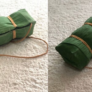 Puede incluir: Un paquete envuelto en verde y marr&oacute;n atado con una cuerda marr&oacute;n. El paquete est&aacute; hecho de hojas de pl&aacute;tano y tiene una textura tejida.