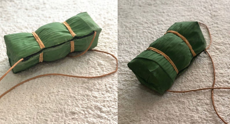 Puede incluir: Un paquete envuelto en verde y marr&oacute;n atado con una cuerda marr&oacute;n. El paquete est&aacute; hecho de hojas de pl&aacute;tano y tiene una textura tejida.