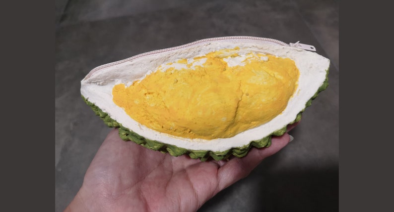 May include: A yellow durian fruit shaped zippered pouch with a green spiky exterior.