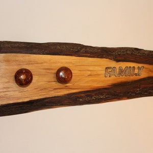 May include: A wooden sign with the word "FAMILY" carved into it. The sign has two brown wooden knobs on the top and a natural wood grain finish.