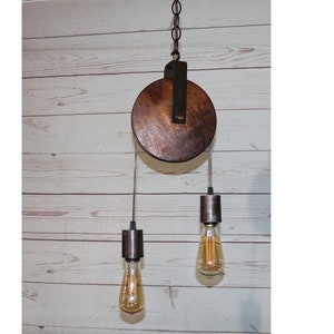 May include: A rustic wooden pulley pendant light fixture with two hanging bulbs. The pulley is made of dark brown wood and has a metal frame. The bulbs are Edison style and have a warm white glow.