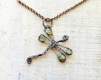 Puede incluir: Un collar de alambre de cobre con un colgante de libélula con piedras preciosas verdes. La libélula está hecha de alambre de cobre y tiene un diseño delicado e intrincado.