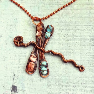 Puede incluir: Un collar de alambre de cobre con un colgante de lib&eacute;lula con piedras turquesa y rosas.