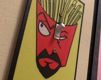 May include: A rectangular light switch cover plate featuring a graphic illustration of a red french fry container with a face, black goatee, and yellow background. The design includes a white toggle switch in the center and two metal screws.
