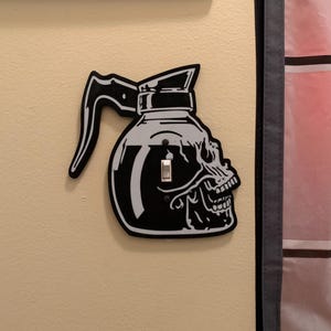 May include: A black and white light switch cover with a skull-shaped coffee pot design.