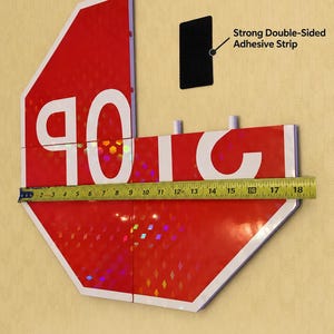 May include: A red octagonal sign with white text reading STOP, composed of four interlocking pieces. A yellow measuring tape shows a width of 18 inches. Includes a black double-sided adhesive strip for wall installation. Text reads Easy Wall Installation and Large Model Approx. 18 inches Wide 4 interlocking pieces.