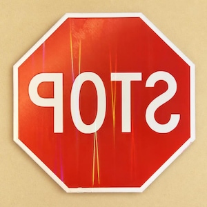 May include: An octagonal red traffic sign with a white border and the word POTS written in large white capital letters. The text is mirrored, appearing as a reflection on the surface of the sign, which features subtle vertical light streaks.