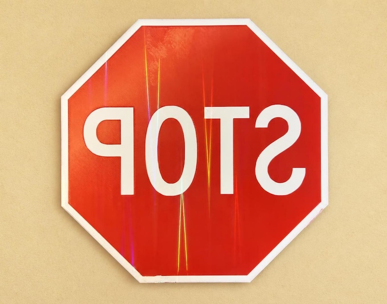 May include: An octagonal red traffic sign with a white border and the word POTS written in large white capital letters. The text is mirrored, appearing as a reflection on the surface of the sign, which features subtle vertical light streaks.