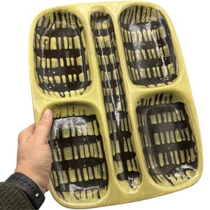 May include: A yellow ceramic serving tray with four compartments. The tray has a black and yellow geometric pattern.