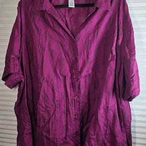 May include: A magenta button-down shirt with a subtle tonal pattern, a classic collar, and three-quarter length sleeves featuring button tabs. The garment includes a front button placket and a Catherines brand label at the inner neckline.