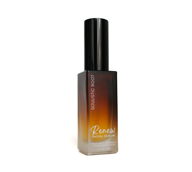 May include: A brown and clear glass bottle of facial serum with a black cap. The bottle has the words "SOULISTIC ROOT" and "Renew FACIAL SERUM" printed on it. The serum is made with Vitamin C and Hyaluronic Acid, and is 1 fl oz / 30ml.