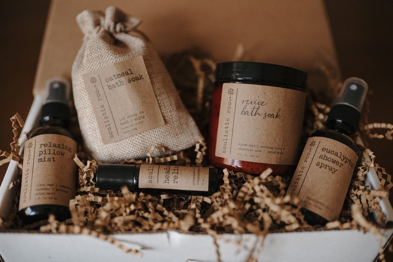 K&ouml;nnte beinhalten: Eine Geschenkbox gef&uuml;llt mit braunen Papierschnitzeln, die eine Auswahl an Bade- und K&ouml;rperpflegeprodukten enthalten. Die Produkte umfassen einen kleinen Jutesack mit der Aufschrift "oatmeal bath soak", ein Glas mit der Aufschrift "revive bath soak", eine Flasche mit der Aufschrift "relaxing pillow mist", eine kleine Flasche mit der Aufschrift "soul head reli" und eine Flasche mit der Aufschrift "eucalyptus shower spray".