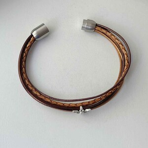 May include: A brown leather bracelet with a silver bee charm and magnetic closures.