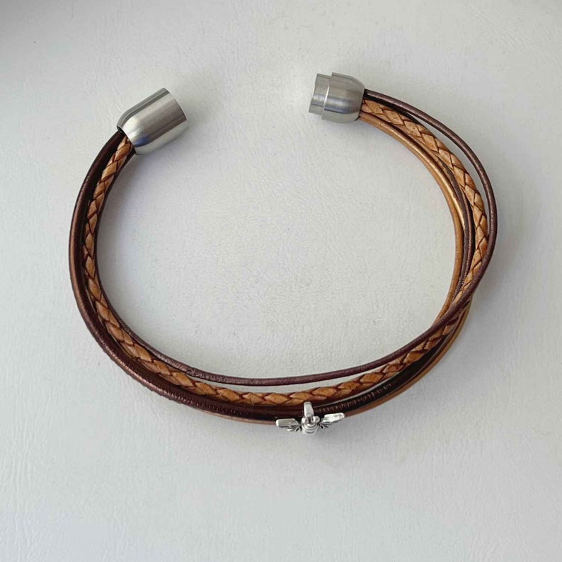 May include: A brown leather bracelet with a silver bee charm and magnetic closures.