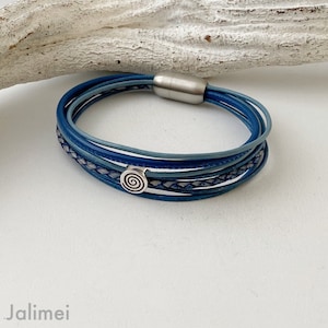 May include: A multi-layered blue leather bracelet with a silver spiral charm. The bracelet is made of several strands of leather, each in a slightly different shade of blue. The spiral charm is attached to the bracelet with a silver clasp.