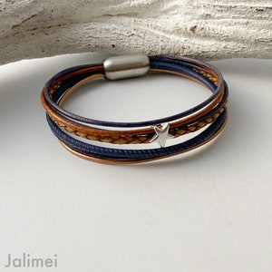 May include: A multi-layered leather bracelet with a silver star charm. The bracelet is made of brown and blue leather and has a silver metal clasp.