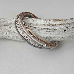 May include: A multi-strand leather bracelet with a braided design and silver beads. The bracelet is in shades of grey, white, and pink.