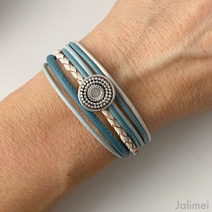 Könnte beinhalten: Ein mehrlagiges Armband mit einem silbernen Knopfverschluss. Das Armband besteht aus einer Kombination aus weißen und blauen Lederriemen.