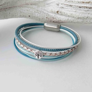 May include: A multi-strand bracelet with a silver tree charm. The bracelet is made of blue and white leather and has a magnetic clasp.