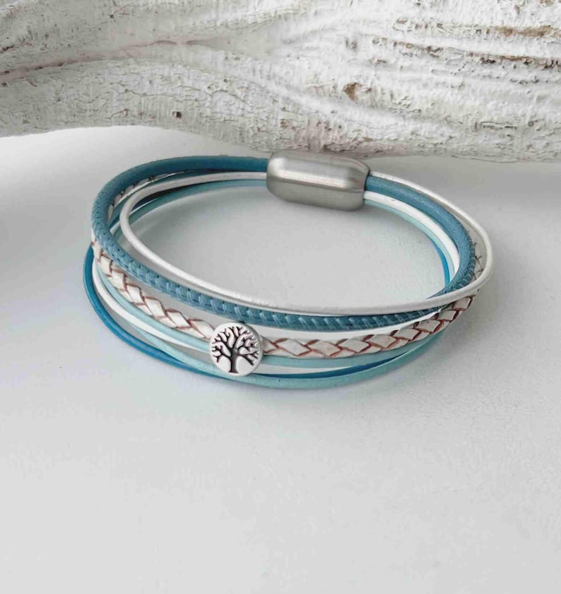 May include: A multi-strand bracelet with a silver tree charm. The bracelet is made of blue and white leather and has a magnetic clasp.