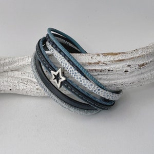 K&ouml;nnte beinhalten: Ein mehrlagiges Lederarmband mit einem Sternanh&auml;nger. Das Armband besteht aus schwarzem, blauem und wei&szlig;em Leder.