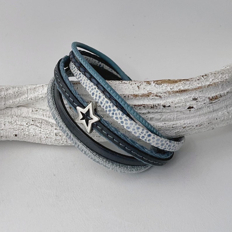K&ouml;nnte beinhalten: Ein mehrlagiges Lederarmband mit einem Sternanh&auml;nger. Das Armband besteht aus schwarzem, blauem und wei&szlig;em Leder.