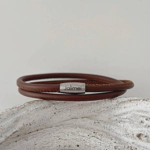 以下が含まれることがあります： マグネットクラスプ付きの茶色の革製ブレスレット。ブレスレットは2本の革紐でできており、クラスプには「Jalimei」の文字が入っています。ブレスレットは白くテクスチャ加工された表面に表示されています。