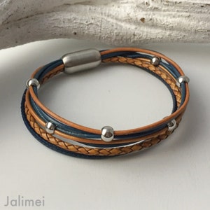 K&ouml;nnte beinhalten: Ein mehrreihiges Lederarmband mit geflochtenem Design. Das Armband verf&uuml;gt &uuml;ber einen silbernen Magnetverschluss und silberne Perlen.