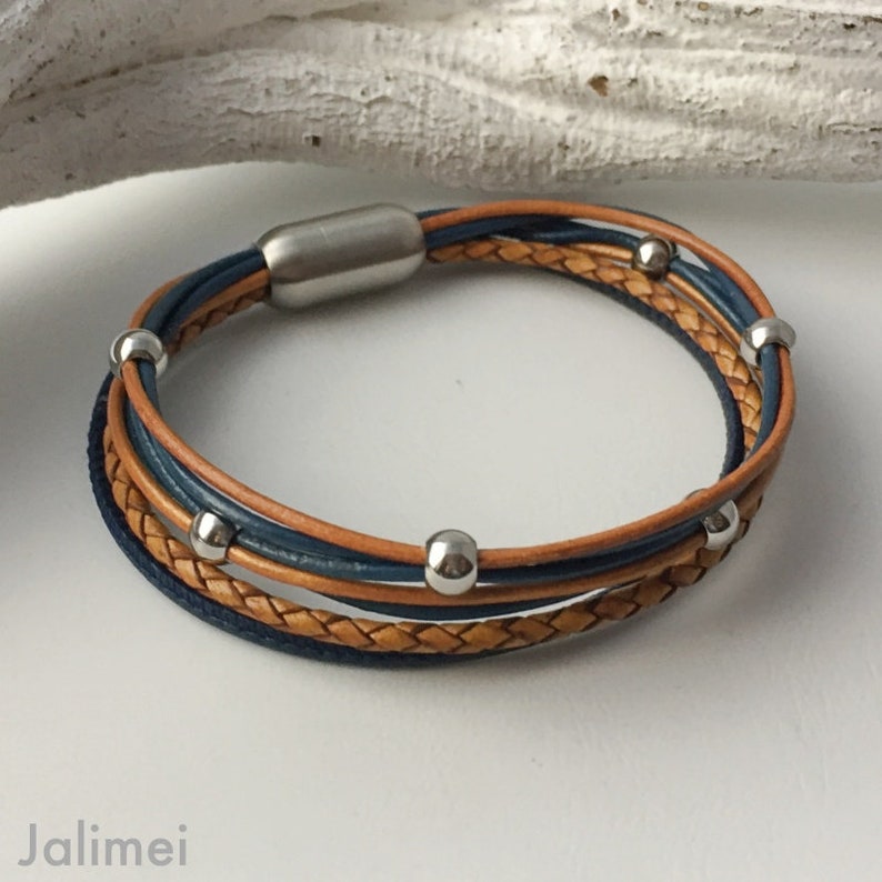 K&ouml;nnte beinhalten: Ein mehrreihiges Lederarmband mit geflochtenem Design. Das Armband verf&uuml;gt &uuml;ber einen silbernen Magnetverschluss und silberne Perlen.