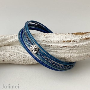 May include: A blue leather bracelet with a silver spiral charm. The bracelet is made of multiple strands of leather, some braided and some smooth.
